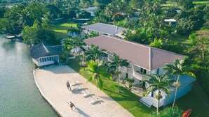 An aerial view of a beachfront property with a large building, a sandy beach, and palm trees.