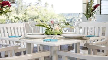 A table set for two with white chairs, a centerpiece of green foliage, and clear glassware.