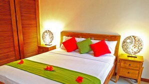 A neatly made bed with a green bedspread and red and green pillows, flanked by wooden nightstands with decorative wall sconces.