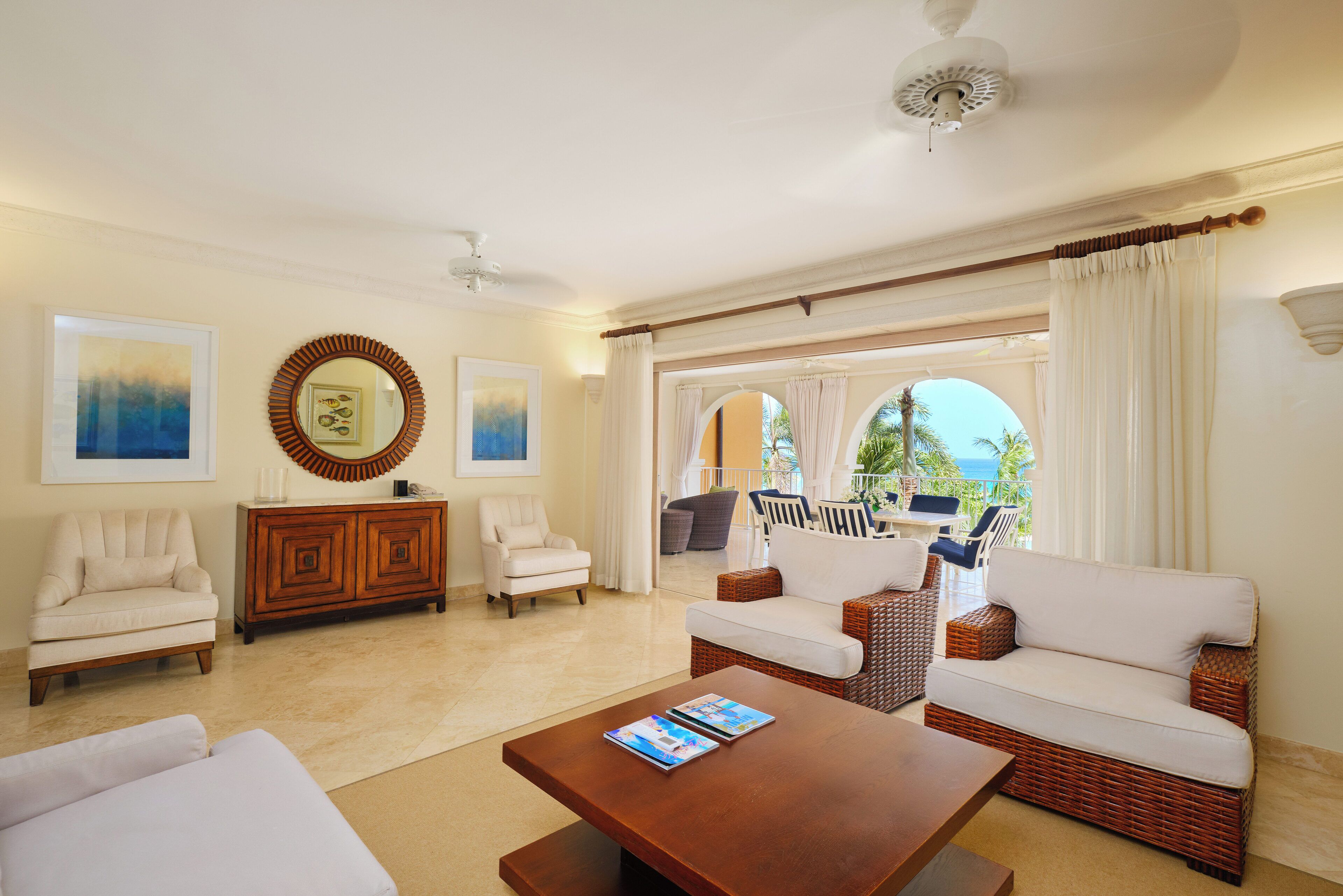 A spacious living room with a large window, a wooden coffee table, and a wicker sofa.