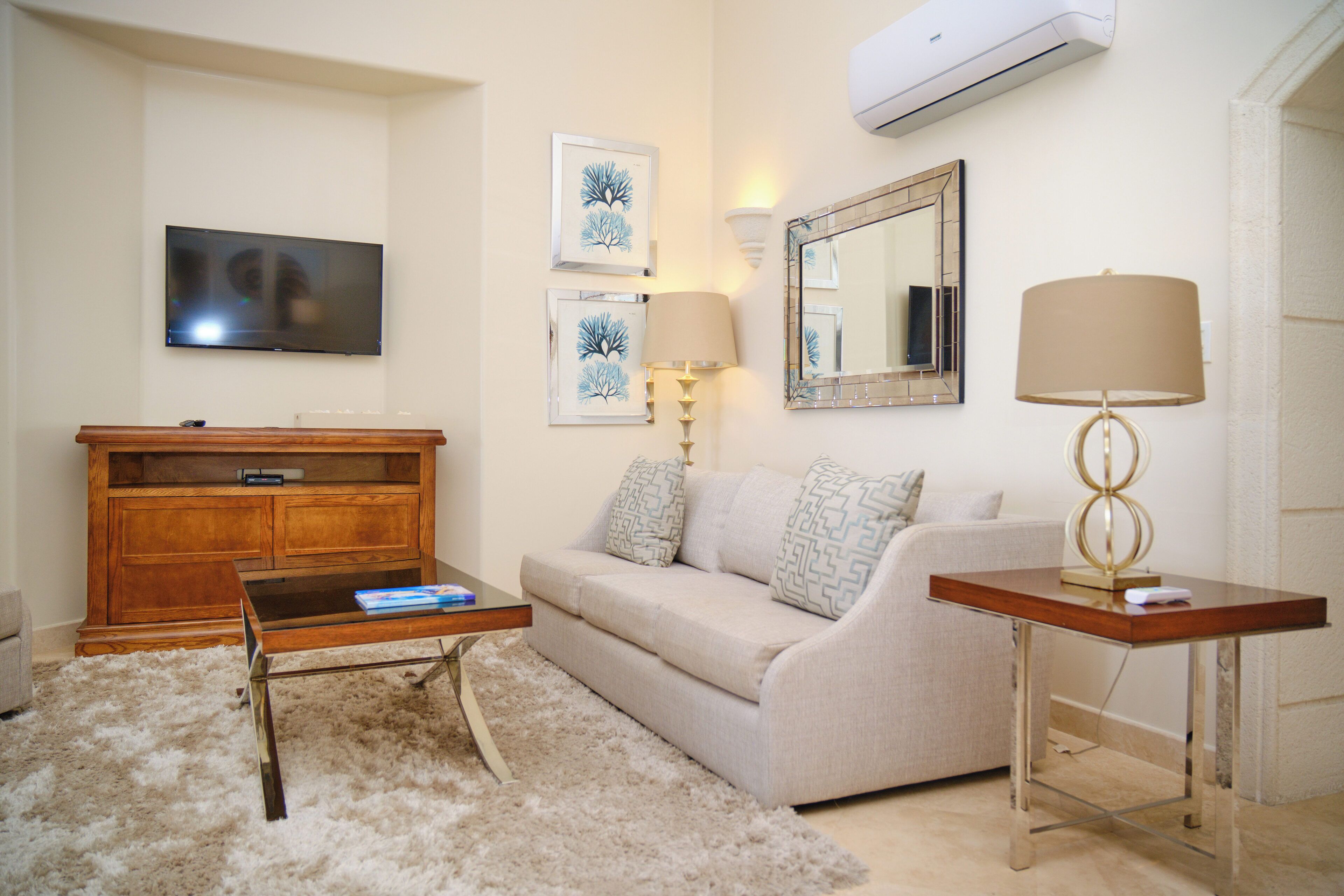 A living room with a flat-screen TV, a wooden entertainment unit, a beige sofa, a coffee table, and a lamp.