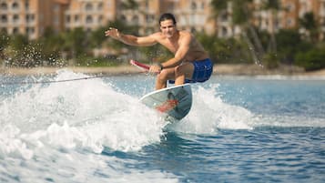 Una persona surfeando una ola con una tabla de surf, vistiendo pantalones cortos azules y un reloj.