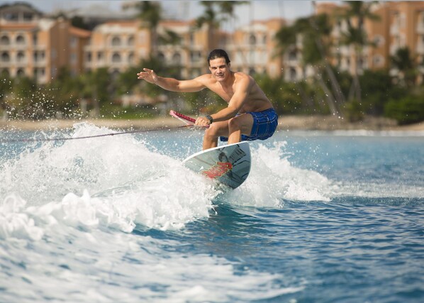 A person surfing on a wave with a surfboard, wearing blue shorts and a watch. - Saint Peter's Bay (Speightstown)