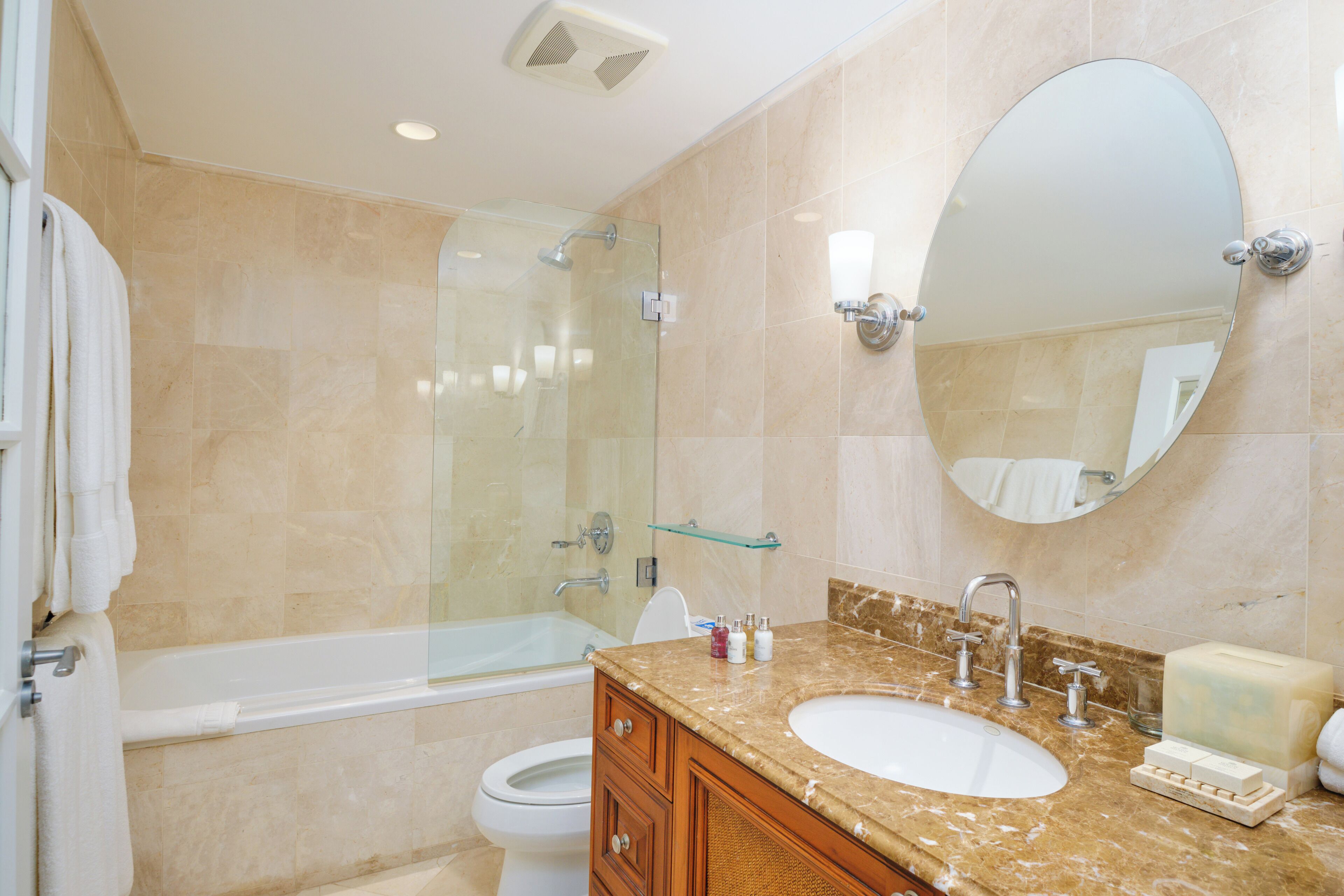 Un baño moderno con ducha envuelta en vidrio, una bañera blanca, un lavamanos con encimera de mármol y un espejo grande.