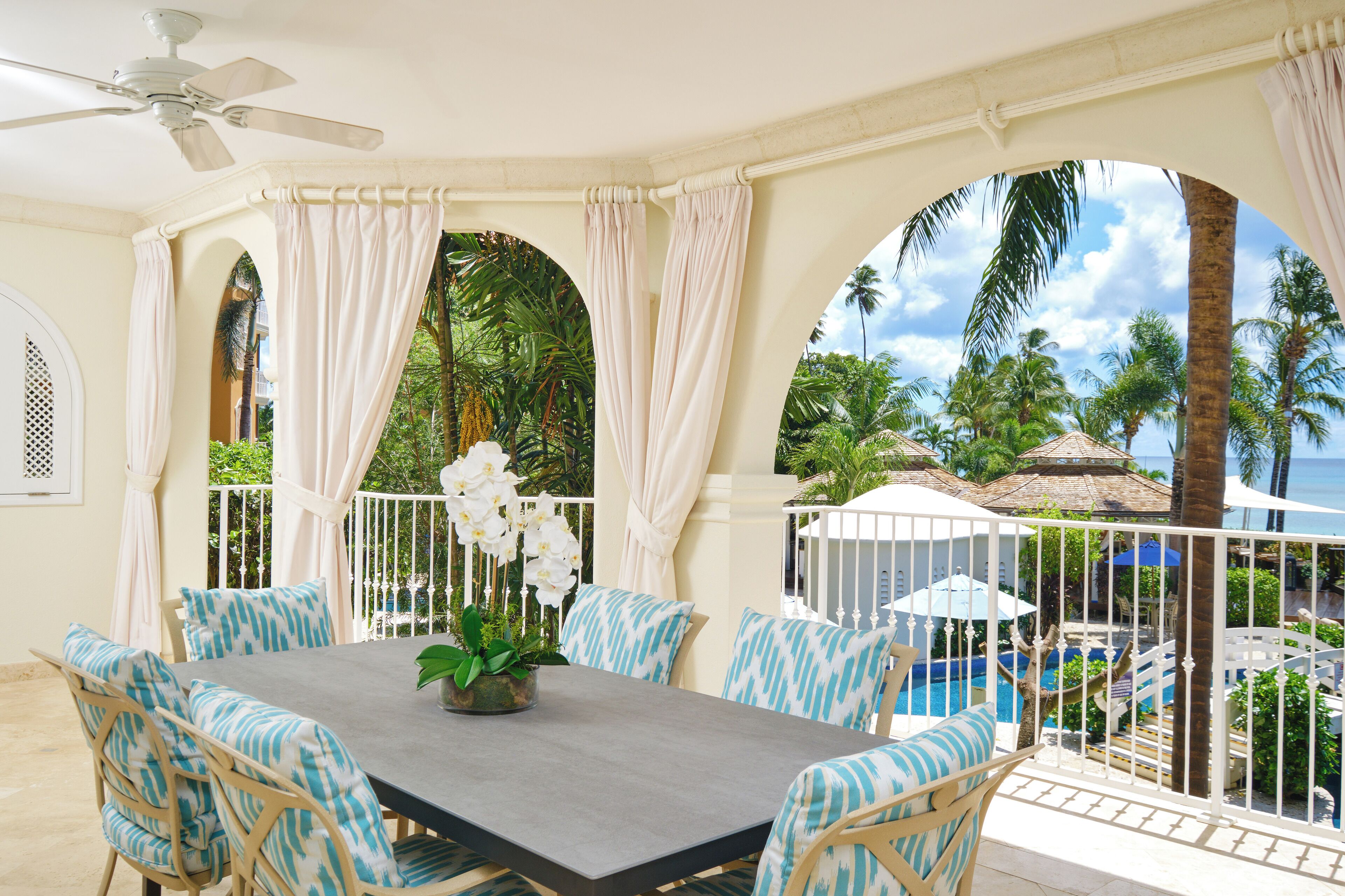 A covered outdoor dining area with a table, chairs, and a ceiling fan.