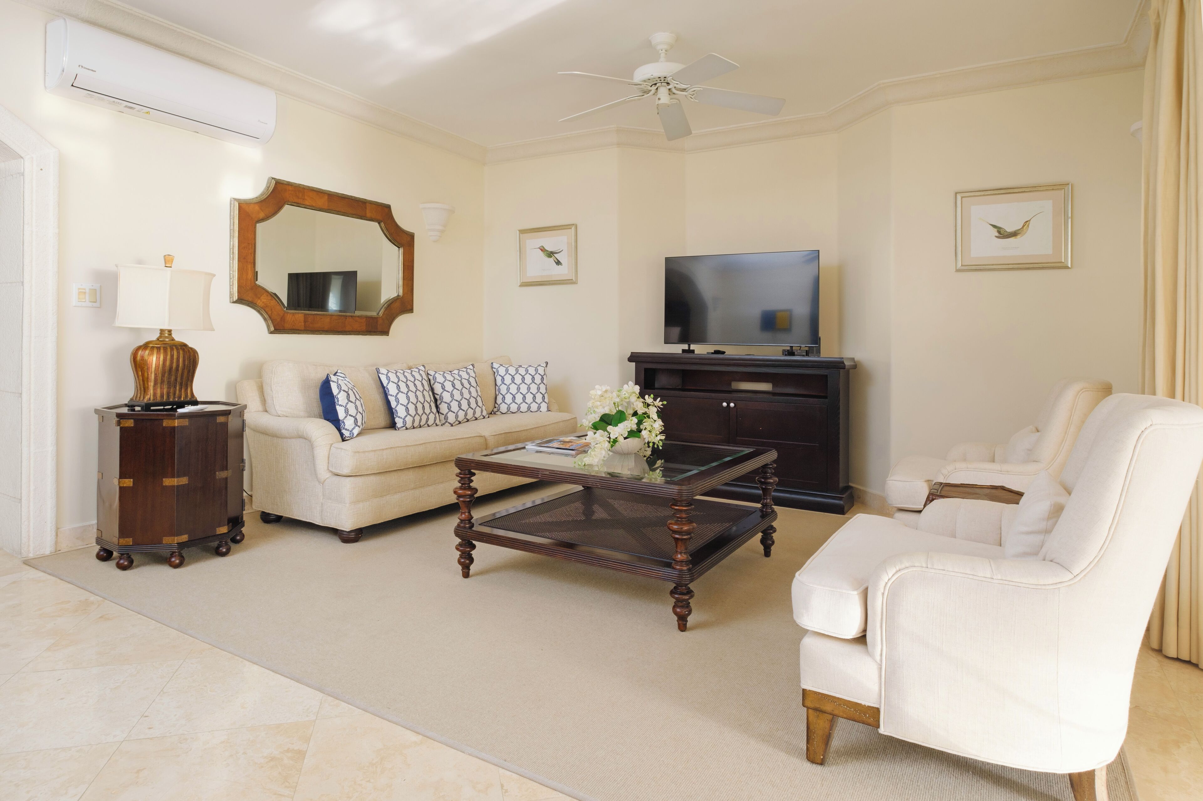 Una sala de estar con sofá, sillón, mesa de centro, televisor y un espejo decorativo.