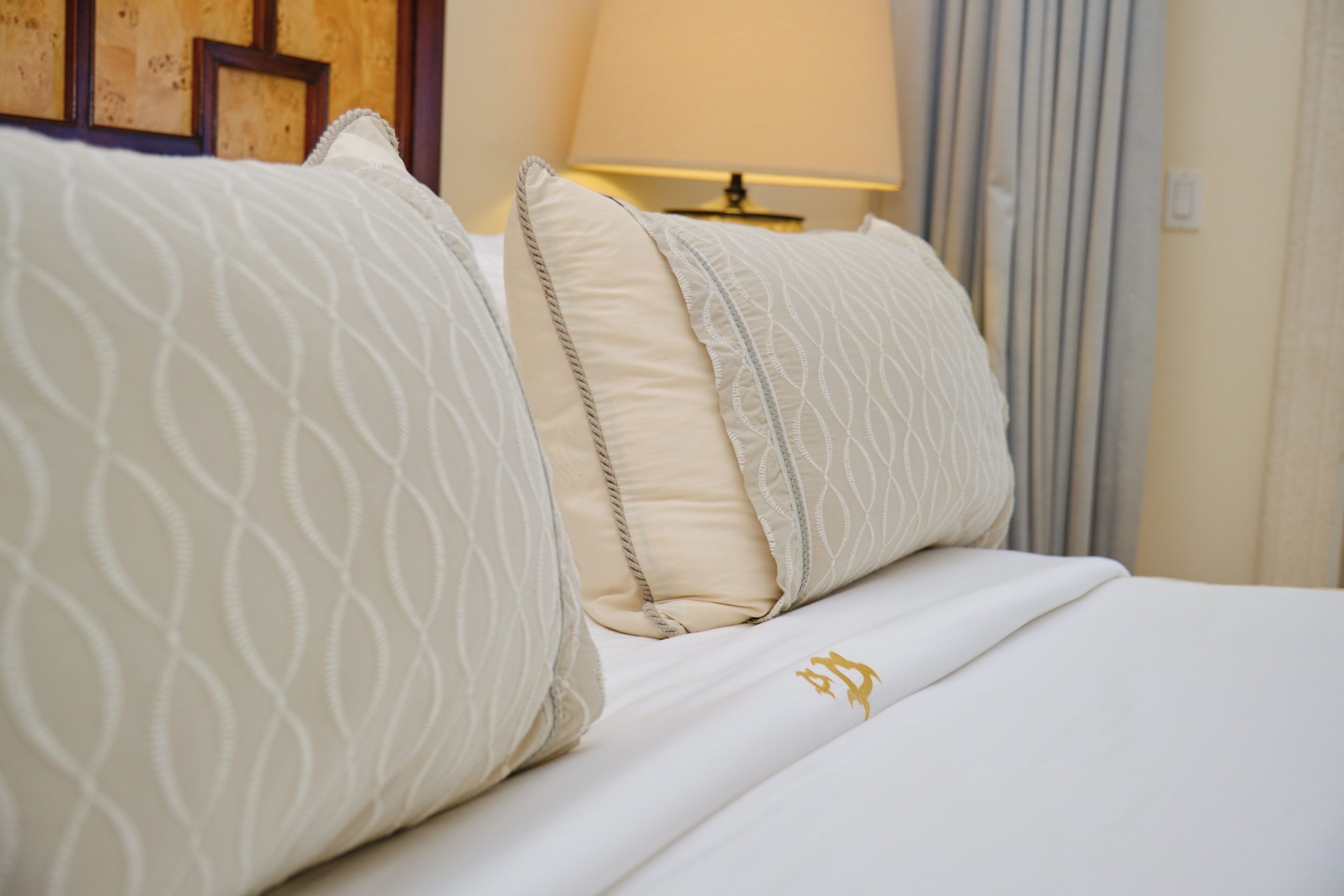 A neatly made bed with patterned pillows and a gold emblem on the bedspread.