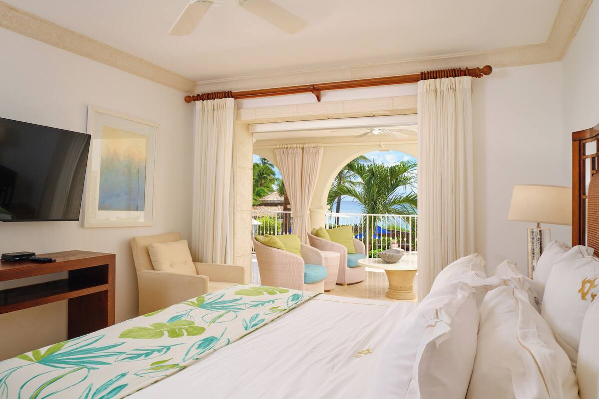 A hotel room with a bed, a TV, a desk, and a balcony with chairs and a table.