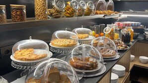 Un bufé con diversos alimentos, incluyendo tartas, pan y frascos con nueces y frutas secas.