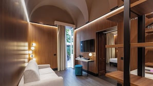 Una habitación de hotel moderna con sofá, escritorio, televisor y armario.