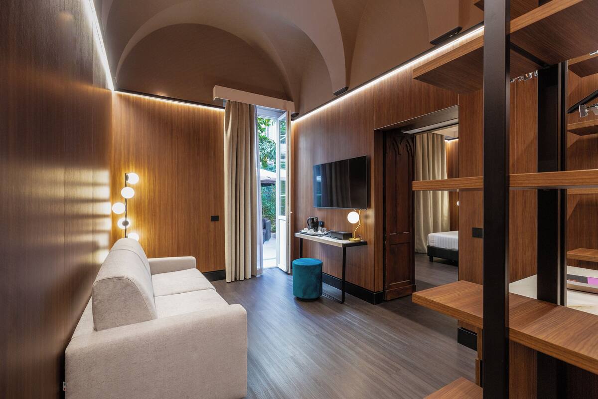 A modern hotel room with a sofa, a desk, a TV, and a wardrobe.