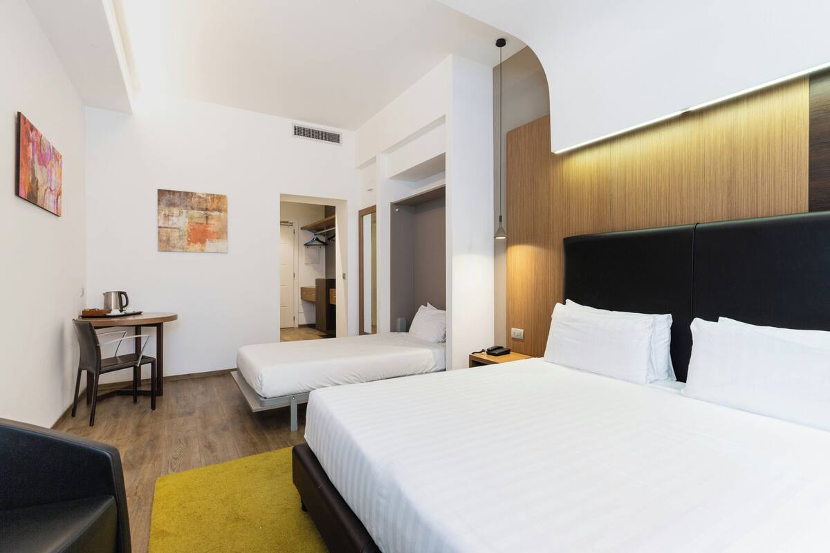 A hotel room with two beds, a desk, a chair, and a coat rack.