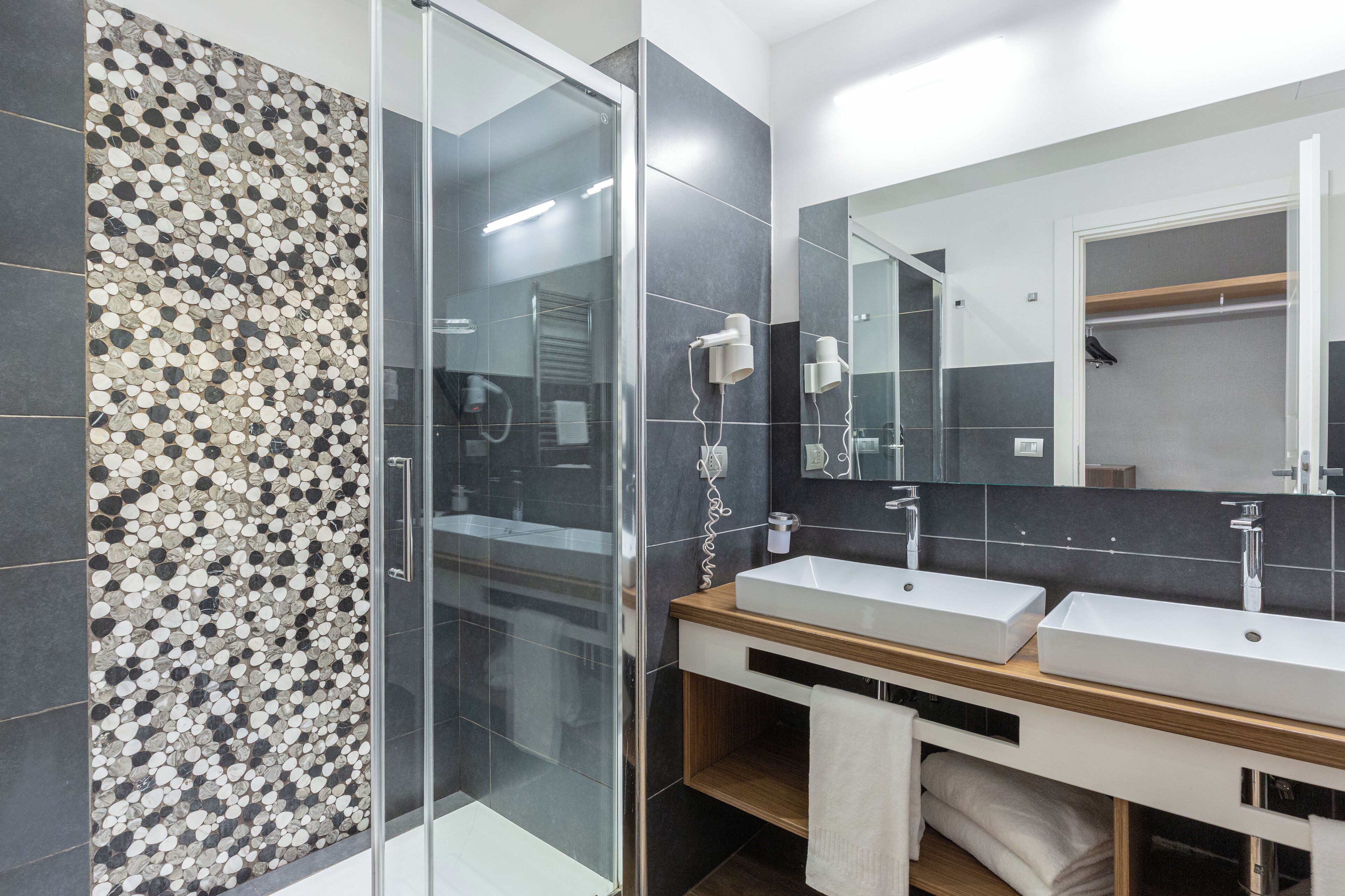 A modern bathroom with a glass shower enclosure, two sinks, and a large mirror.