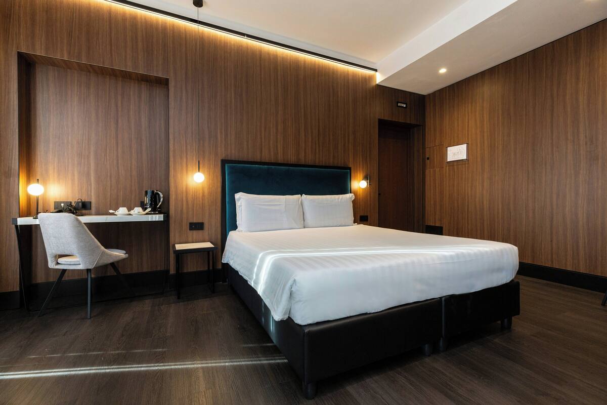 A modern hotel room with a large bed, a desk, and a chair.