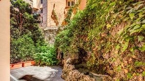 Un patio estrecho con fuente de agua, paredes de piedra y plantas en macetas.