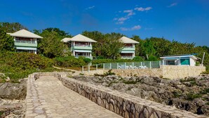 A pathway leading to a resort with multiple buildings, each featuring a balcony and surrounded by lush greenery. - Idle Awhile Cliffs (Negril)