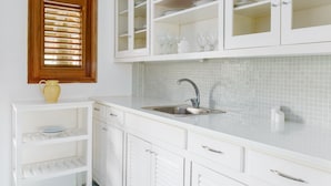 A kitchen with white cabinets, a sink, and a window with blinds.