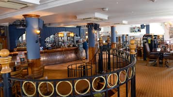 A bar area with a curved staircase, wooden furniture, and a variety of bottles on shelves.