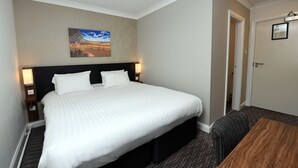A hotel room with a large bed, two bedside lamps, a wooden nightstand, a framed picture on the wall, and a door with a sign. - Wynnstay Arms, Wrexham by Marston's Inns (Wrexham)