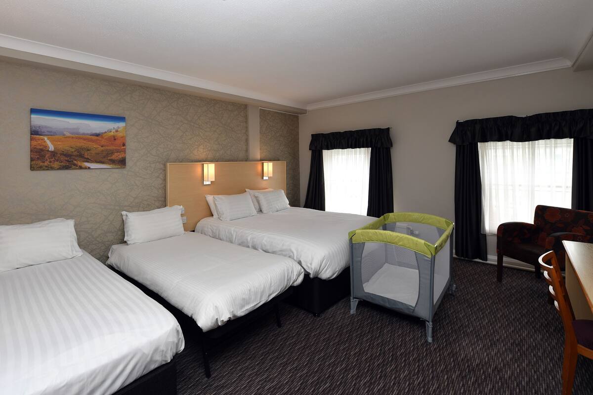 A hotel room with three beds, a small table, a chair, and a window with curtains.