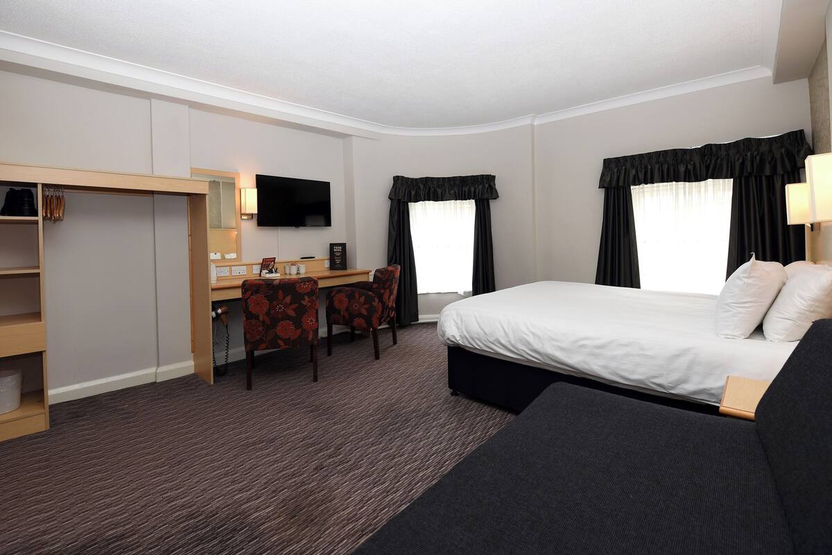 A hotel room with a bed, a desk with a chair, a wardrobe, and a TV.
