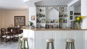 Zona de bar con armarios blancos, taburetes verdes y una variedad de botellas de licor.