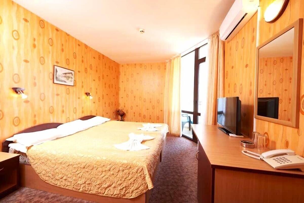 A hotel room with a bed, a desk with a telephone, a television, and a large window.