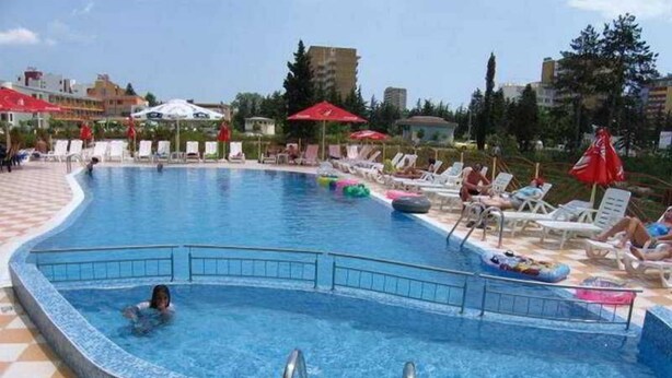 A swimming pool with lounge chairs and umbrellas, surrounded by buildings. - Smolian (Nessebar)