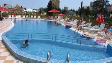 Una piscina con sillas de descanso y sombrillas, rodeada de edificios.
