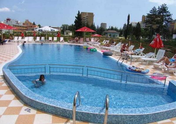 A swimming pool with lounge chairs and umbrellas, surrounded by buildings.