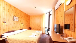 A hotel room with a bed, a desk with a telephone, a television, and a large window. - Smolian (Nessebar)