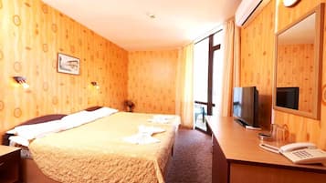 Habitación de hotel con una cama, un escritorio con teléfono, televisión y un ventanal grande.