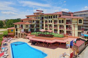 A hotel with multiple balconies, a swimming pool, and outdoor seating areas.
