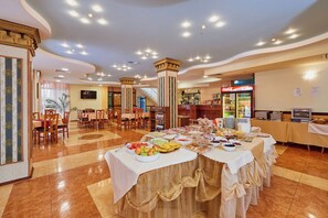 A buffet setup with various food items, a Coca-Cola refrigerator, and a seating area with tables and chairs.