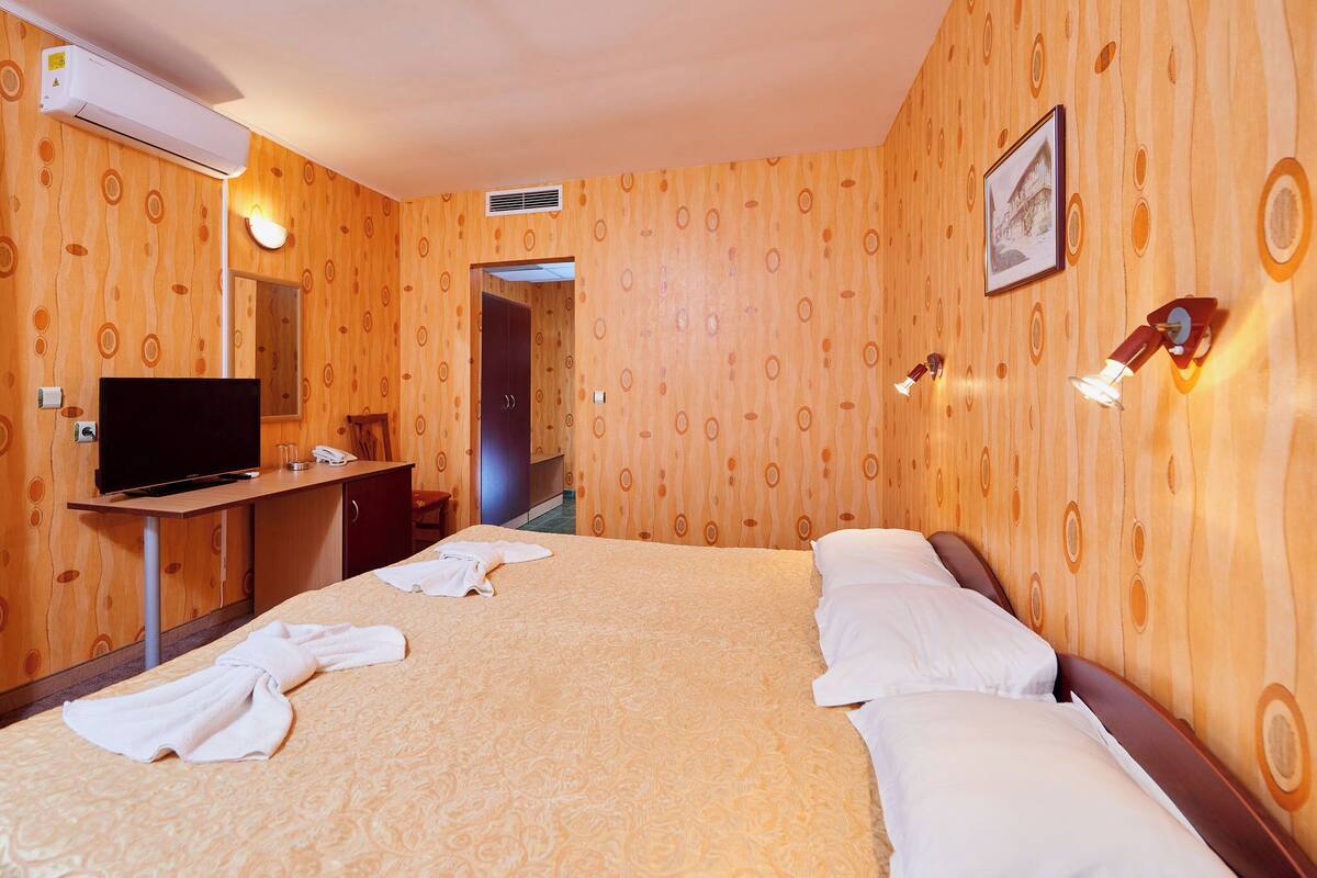 A hotel room with a wooden-patterned wall, a bed with white linens, a television on a desk, and a framed picture on the wall.