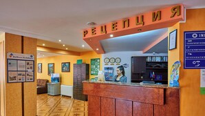 A hotel reception area with a wooden reception desk, a sign with Cyrillic text, a wall clock, and a framed picture. - Smolian (Nessebar)