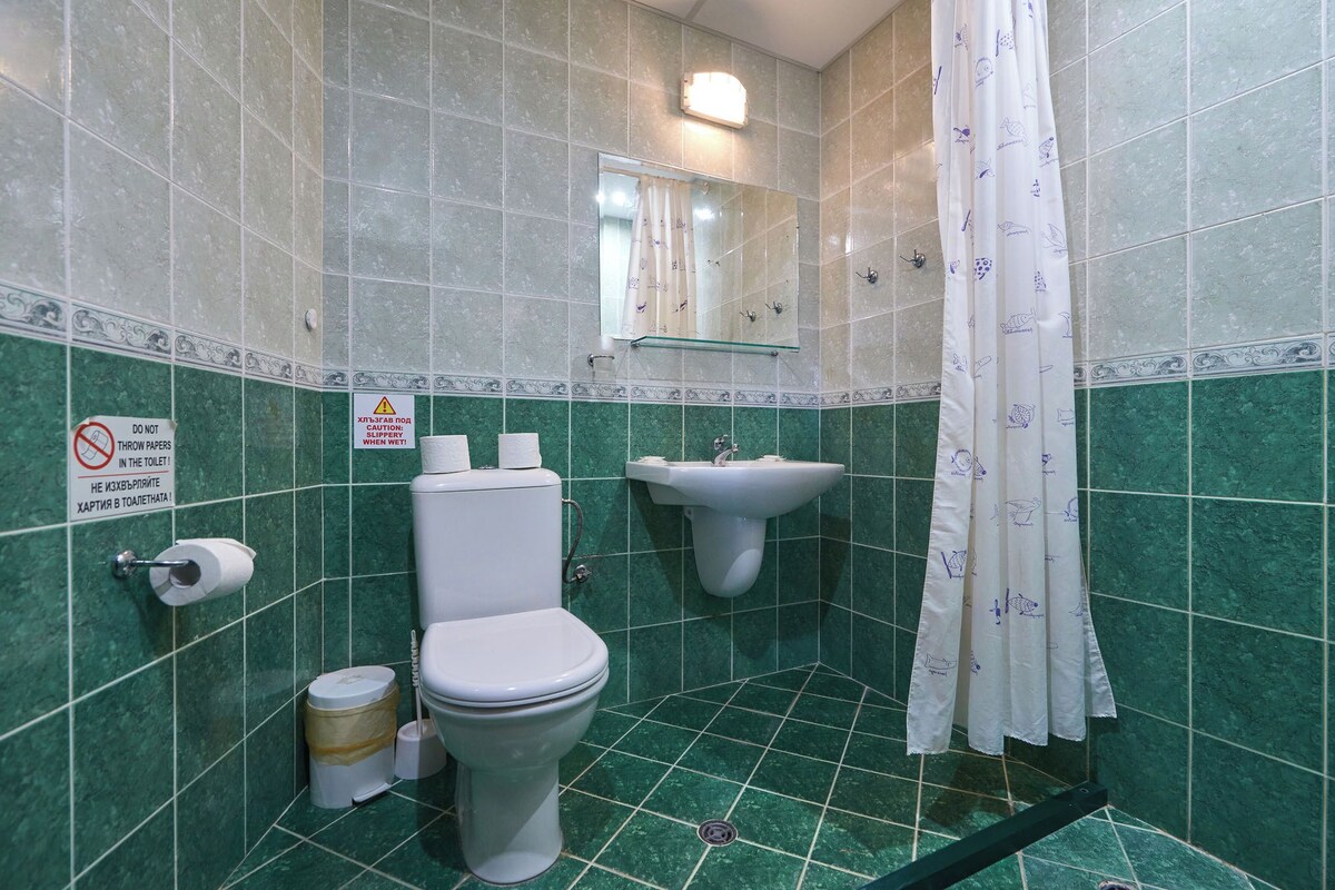 A bathroom with green tiles, a toilet, a sink, and a shower curtain.