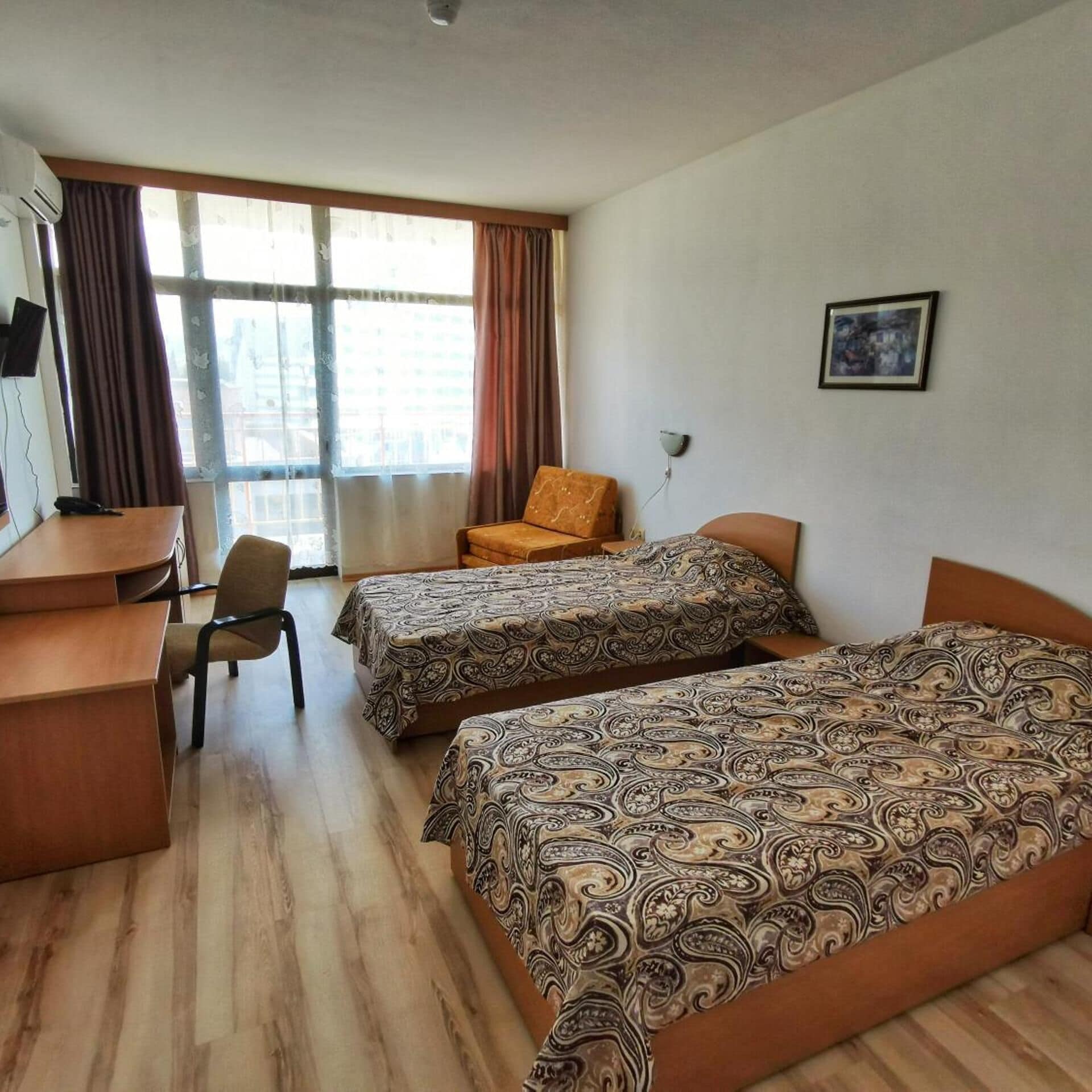 A hotel room with two beds, a desk, a chair, and a window with curtains.