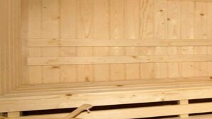 Interior de una cabaña de madera con techo inclinado y un banco a lo largo de la pared.