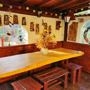 Eine Sitzgruppe mit Holzbänken, einem Tisch, einer Vase mit Blumen und Wandbildern.