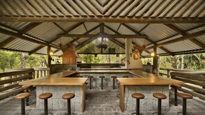 Un espace bar extérieur avec une longue table en bois et de nombreux tabourets.