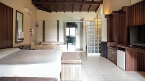 Une chambre d’hôtel avec un grand lit, une télévision, un petit réfrigérateur et une salle de bain visible à travers une porte ouverte.