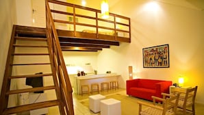 A loft-style apartment with a wooden staircase, a red sofa, and a kitchen area with stools. - Hotel Villaoeste (Mossoro)