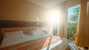 A hotel room with a large bed, a nightstand, and a window with curtains. - Hotel Villaoeste (Mossoro)