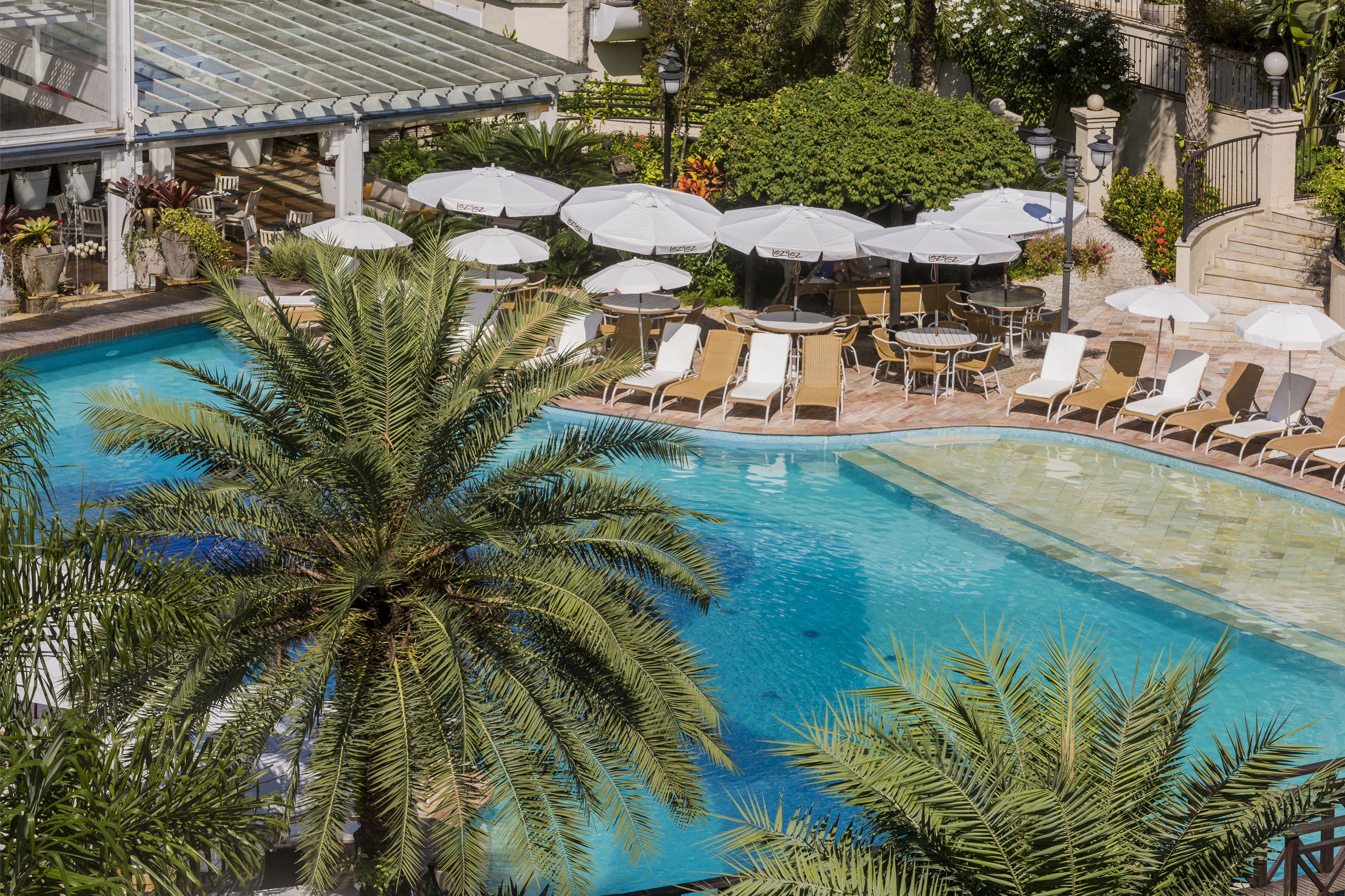 A pool area with lounge chairs and umbrellas, surrounded by palm trees and a covered seating area.