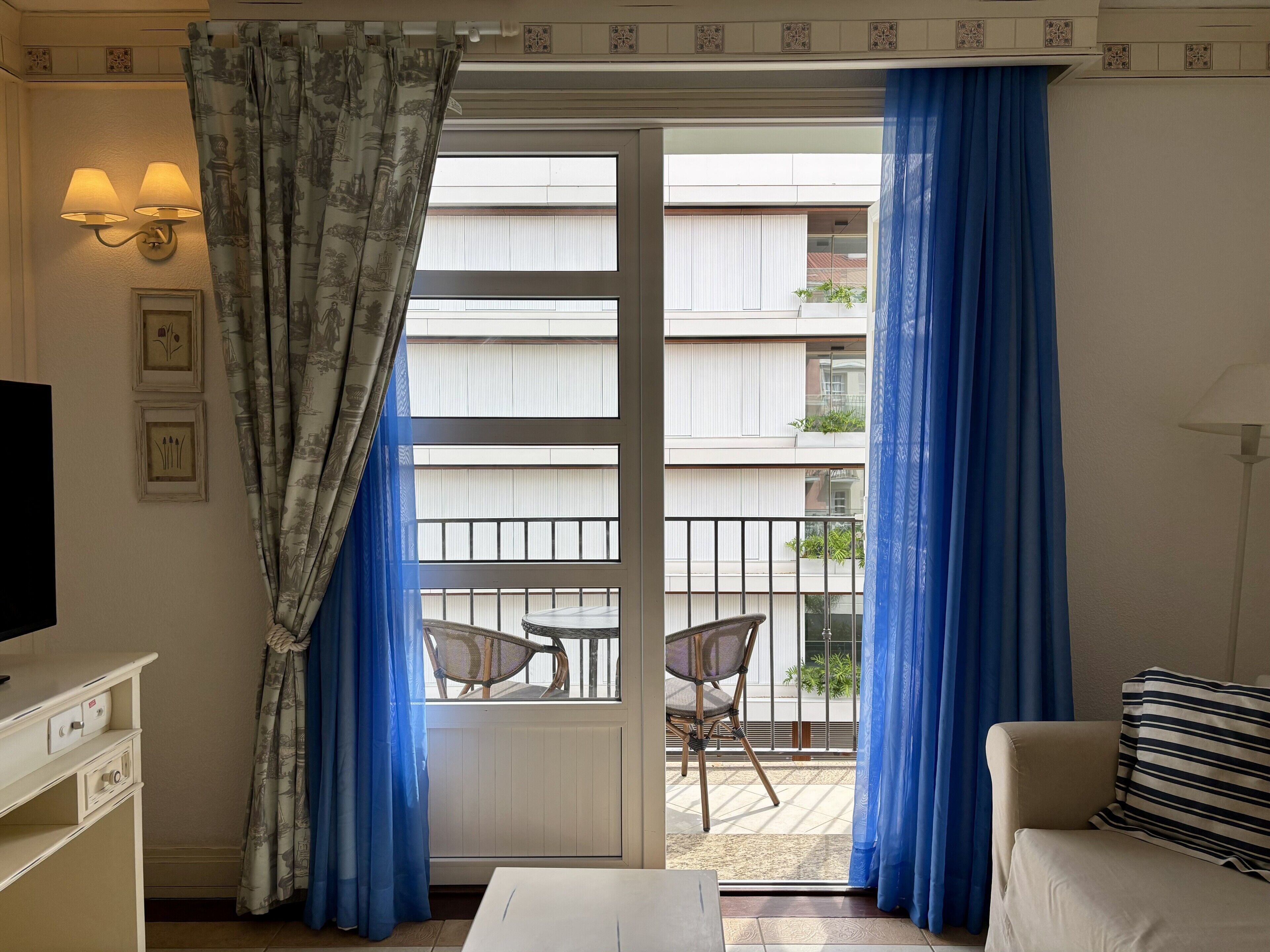 Ein Zimmer mit einer Schiebetür zum Balkon, einem weißen Sofa, einem kleinen Tisch und einem Fernseher auf einem Schrank.