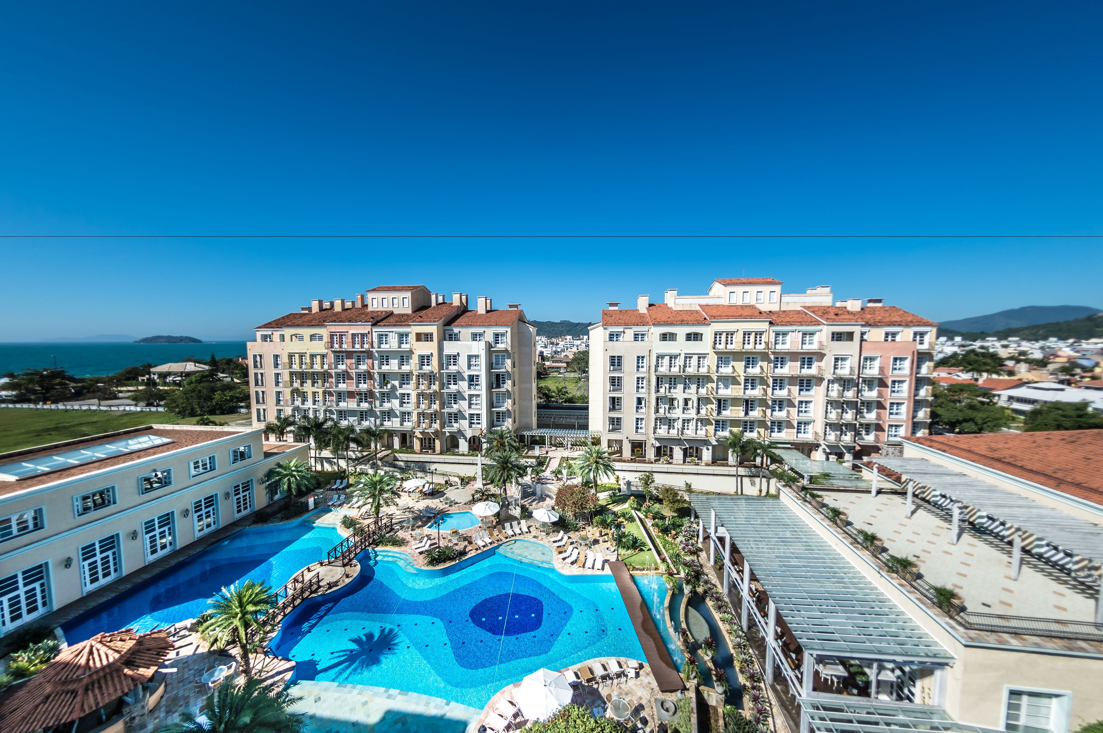 A hotel with a large swimming pool, multiple balconies, and a view of the sea.