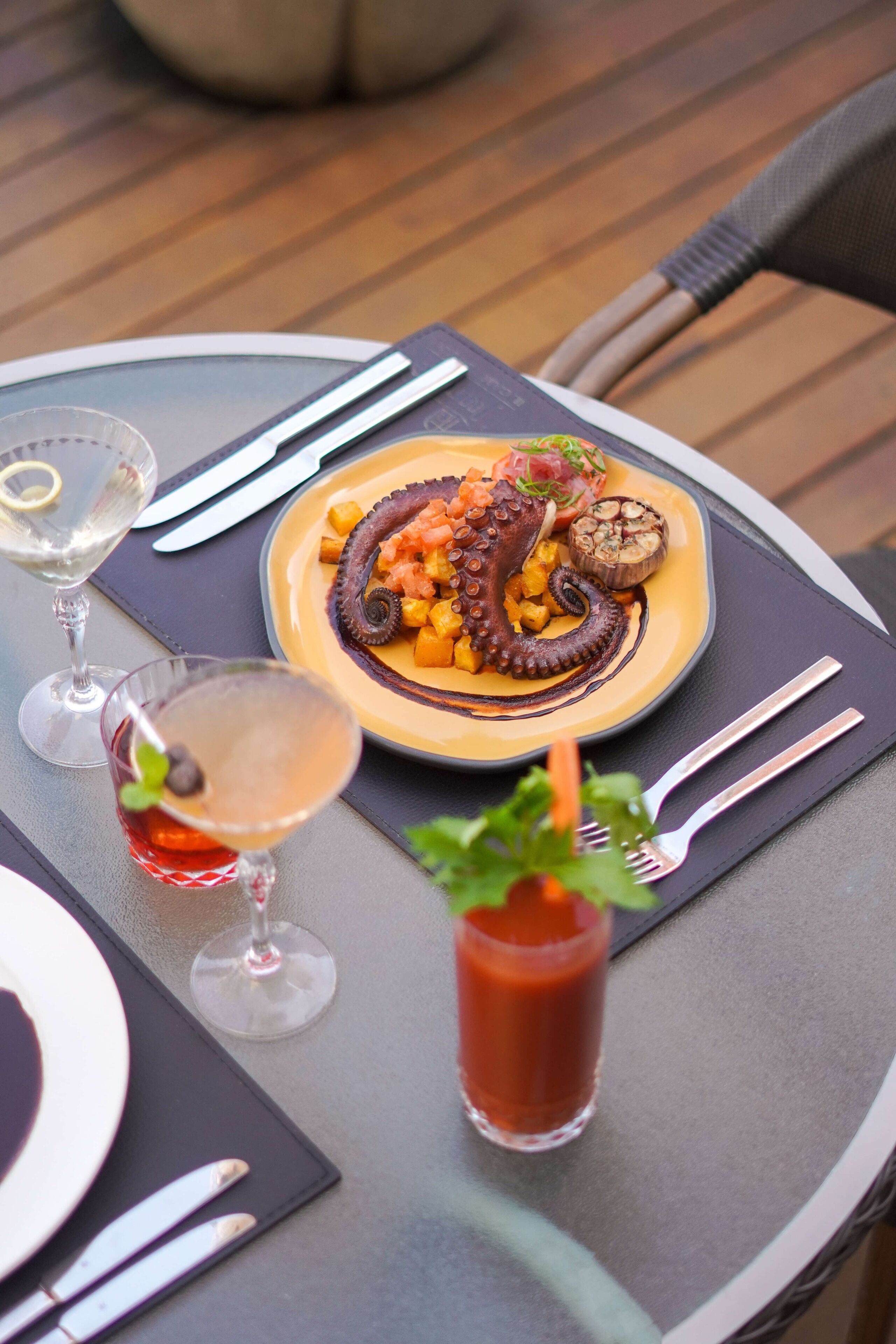 A dining table with a plate of octopus dish, a cocktail, and a glass of red drink.