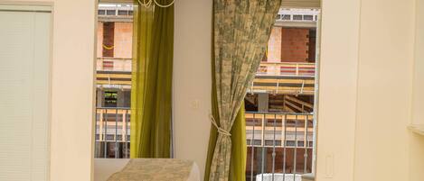 A bedroom with a bed, a window with green curtains, a balcony with a railing, and a chandelier.