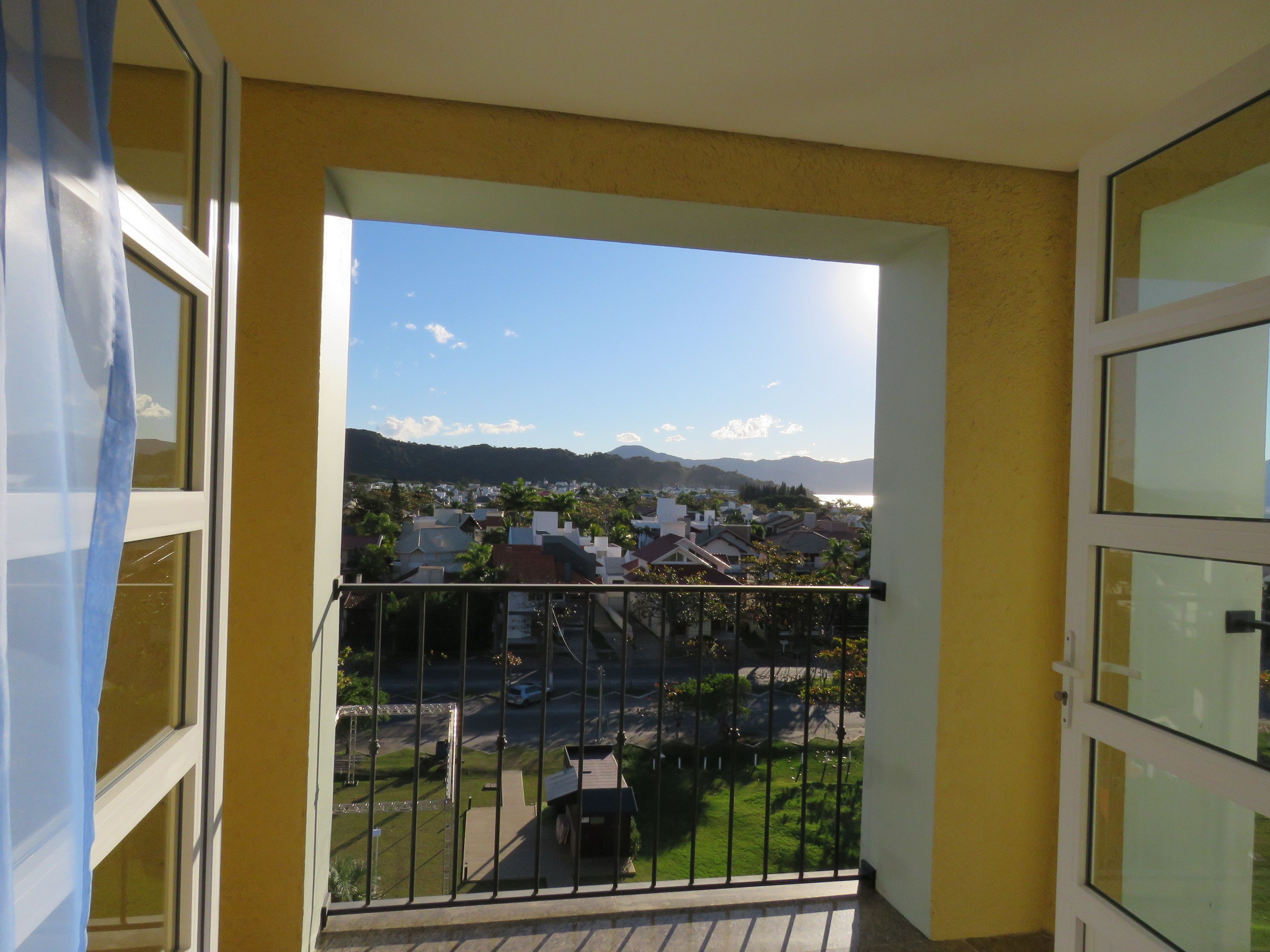A balcony with a metal railing, a view of a residential area with houses and greenery, and a clear sky.